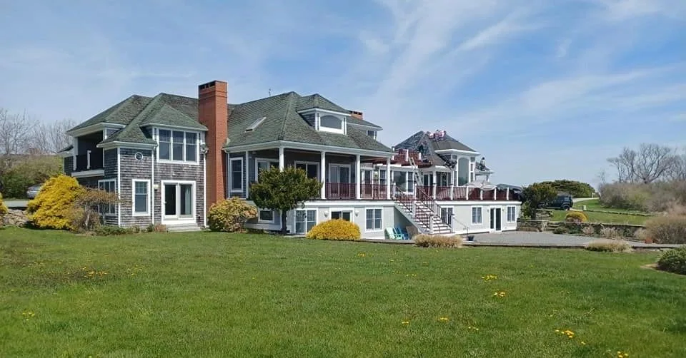 Large shingled home with roofers working on the upper roof